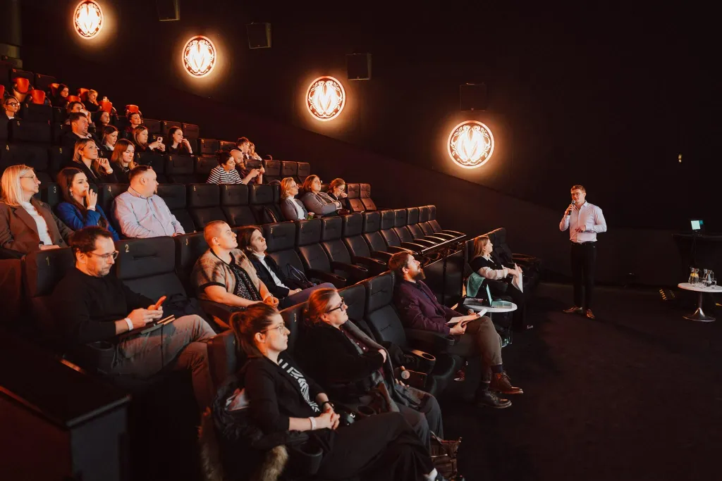 Prelegent przemawia do uczestników konferencji marketingowej w sali kinowej, publiczność siedzi na widowni i słucha prezentacji o digital marketingu.